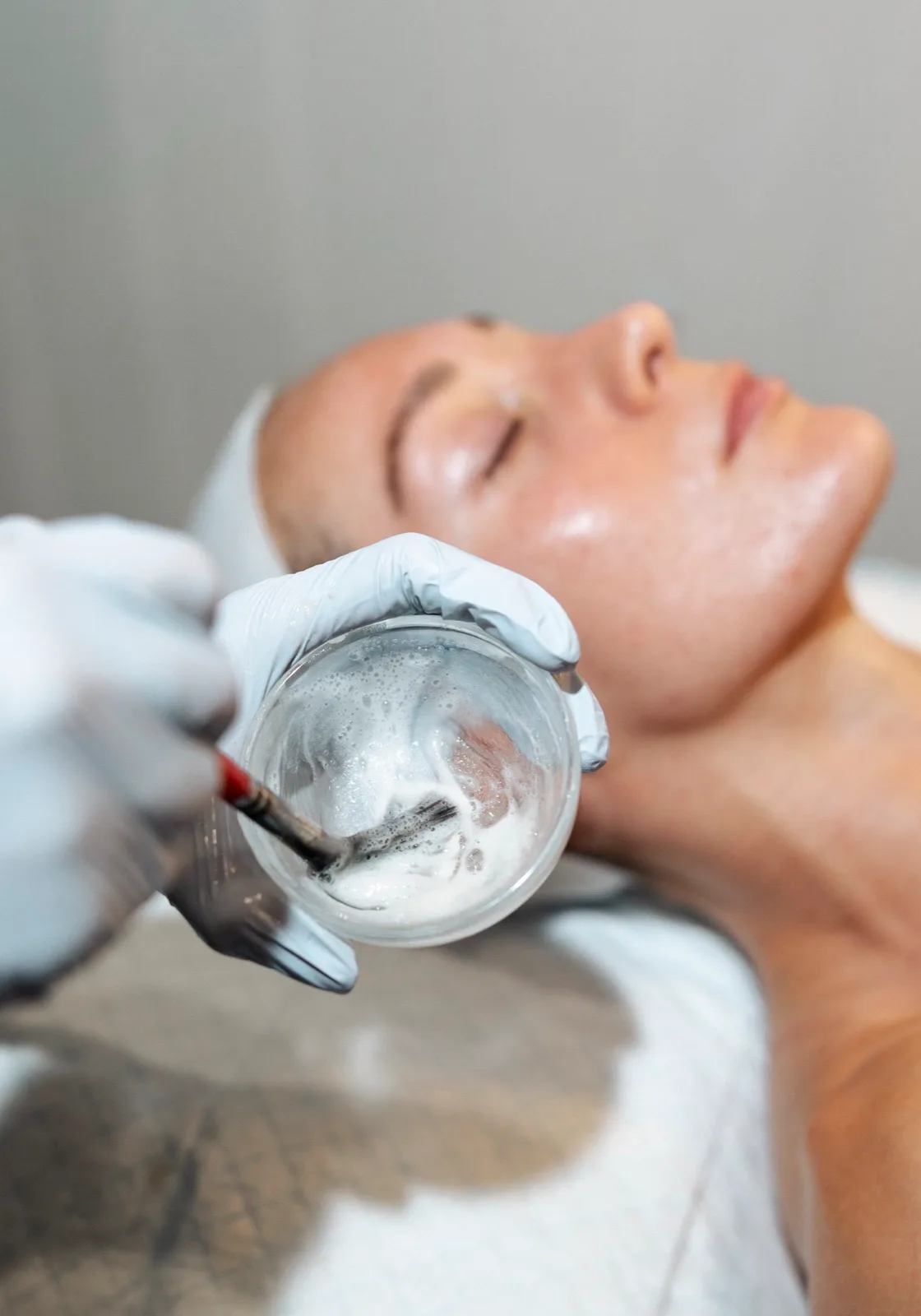 A clinician mixing a clinical peel beside a reclining patient
